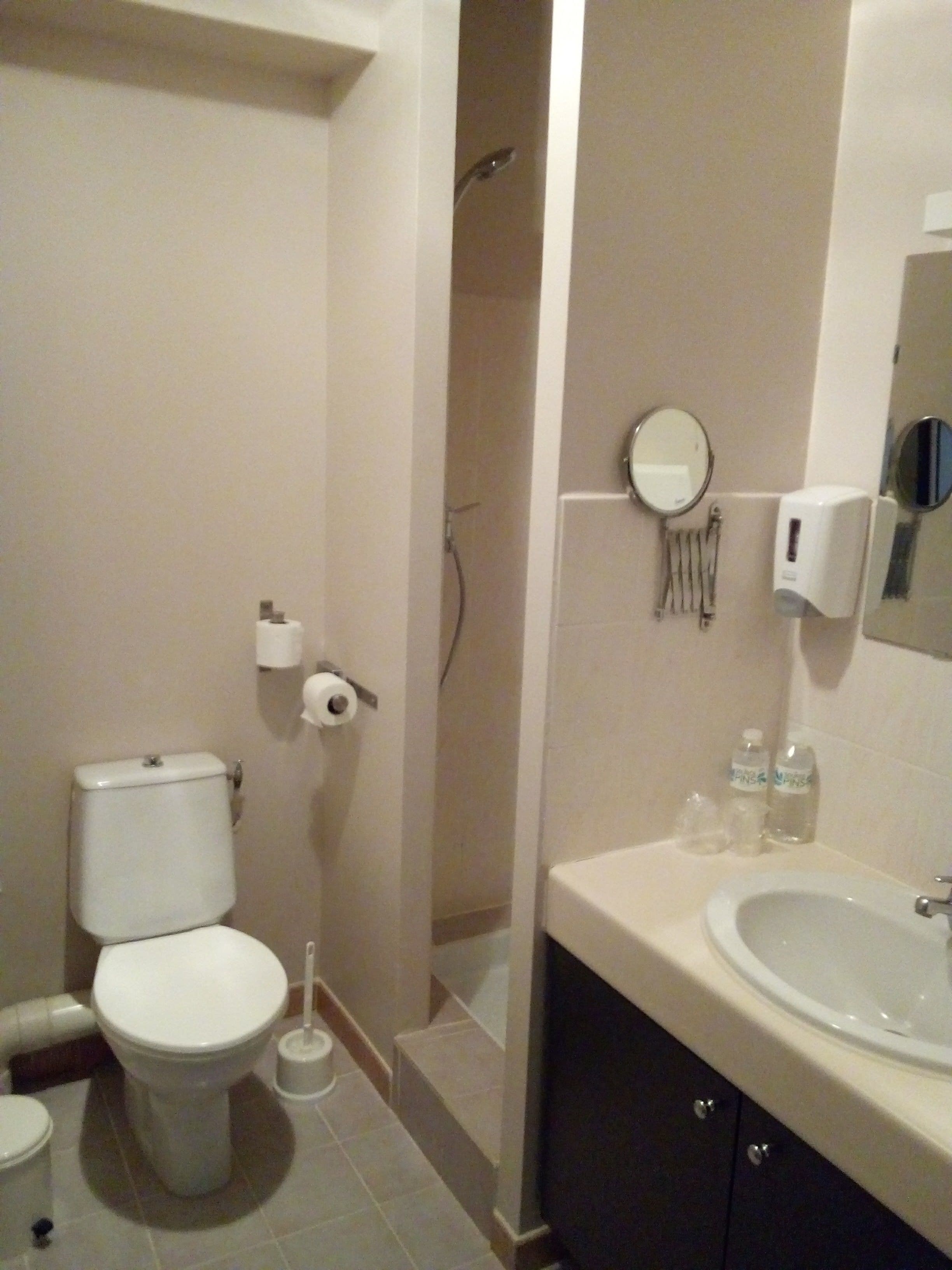 Un baño con inodoro, bidé, lavamanos, espejo y dispensador de toallas.