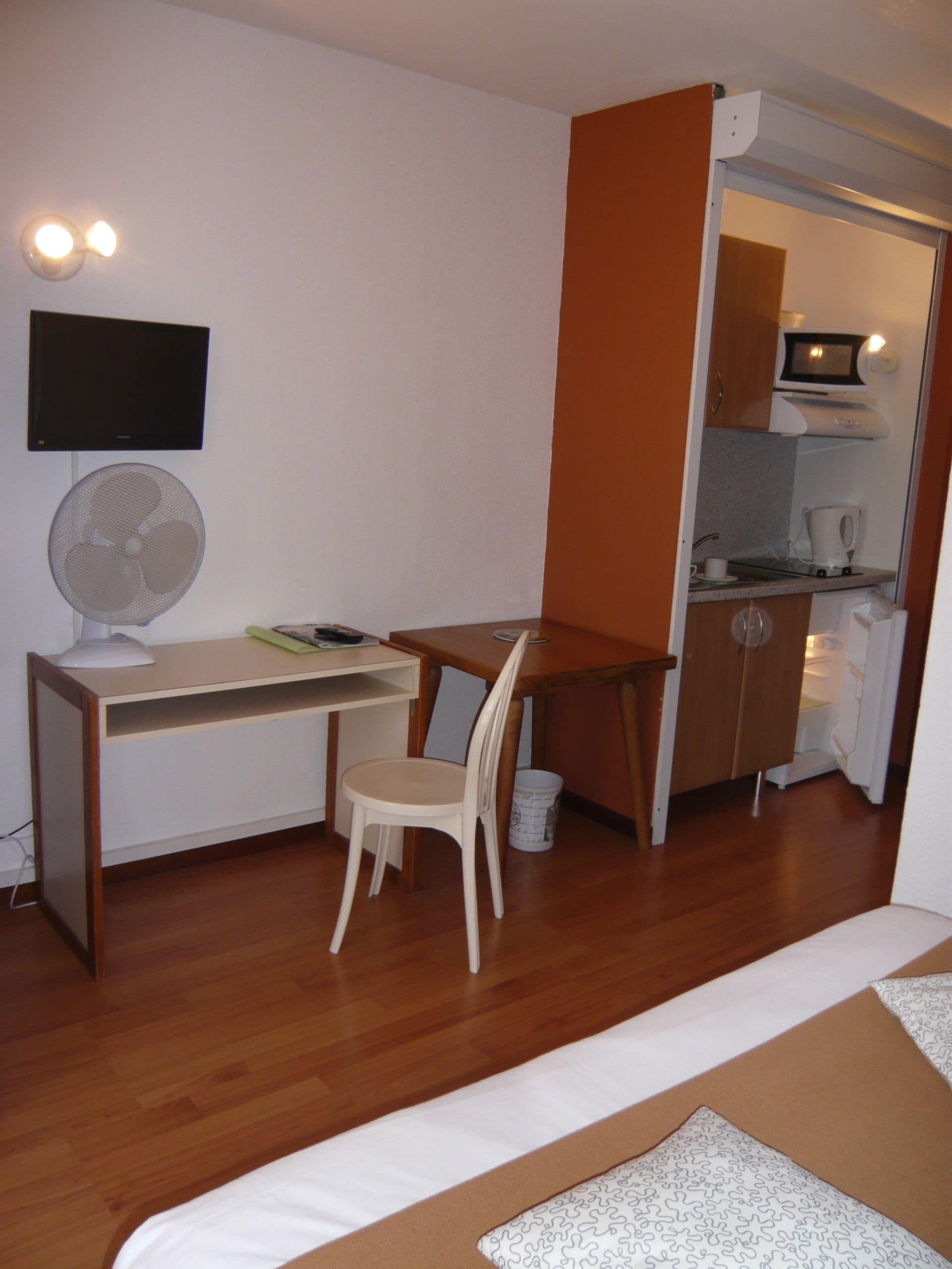 Una habitación pequeña con escritorio, silla y kitchenette.