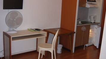 Una habitación pequeña con escritorio, silla y kitchenette.