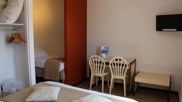 A hotel room with a bed, two pillows, a bedside table, a chair, a desk, a television, and a wardrobe.