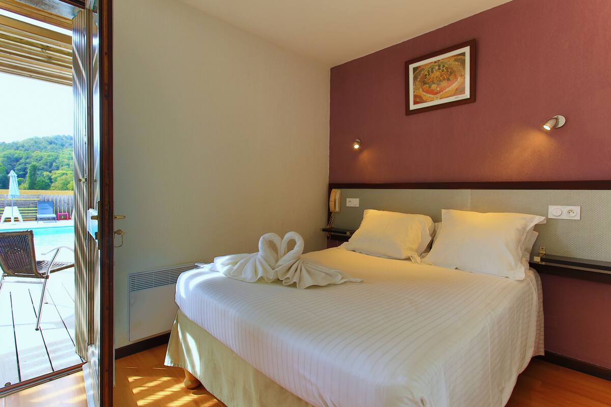 Habitación de hotel con cama, un cuadro en la pared y vistas a una piscina y montañas.