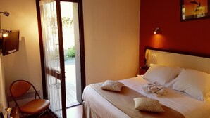 A hotel room with a bed, a chair, a desk, and a door leading to an outdoor area.