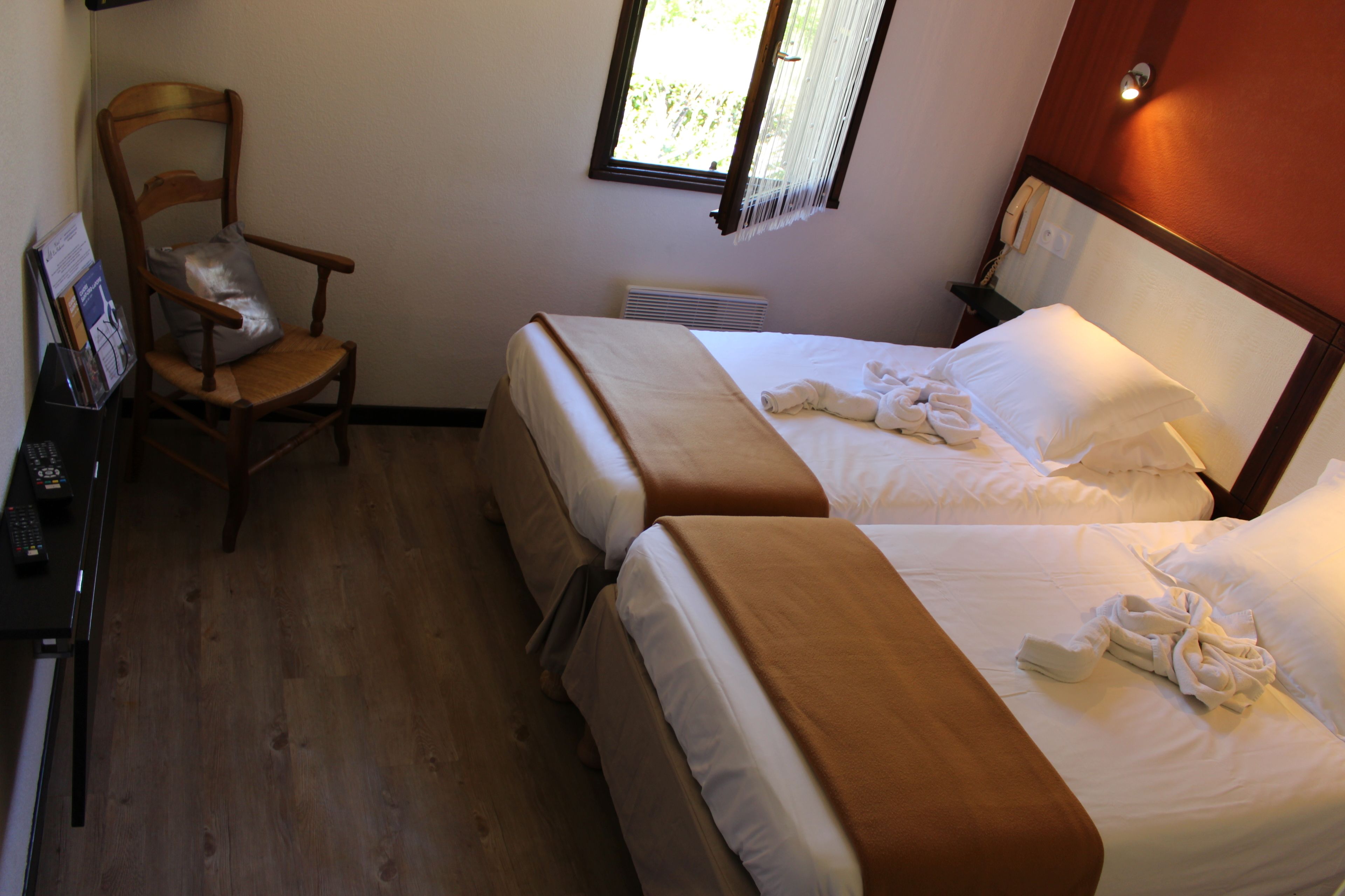 Habitación de hotel con dos camas, una silla de madera, un escritorio con teléfono y una ventana.