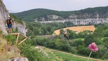A rope bridge over a valley with a person standing on the edge and another in mid-air.
