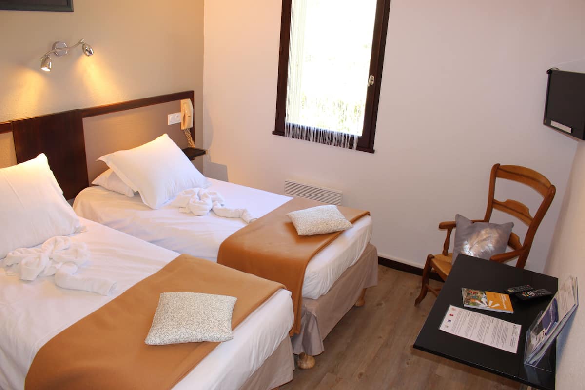 Habitación de hotel con dos camas, una silla, una mesa con un control remoto y una ventana con cortinas.