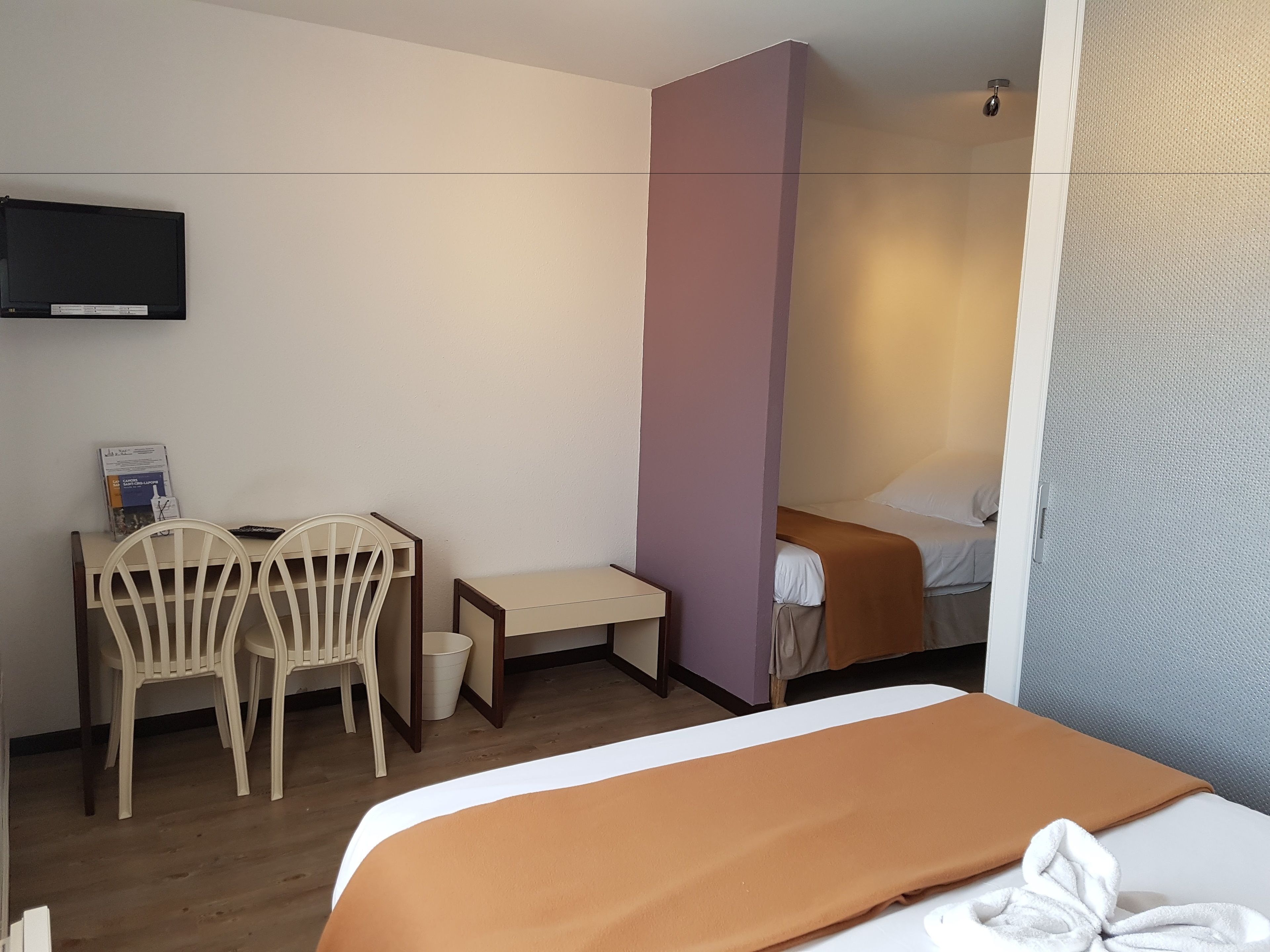 Et hotelværelse med seng, skrivebord, to stole, fjernsyn og et lille bord.
