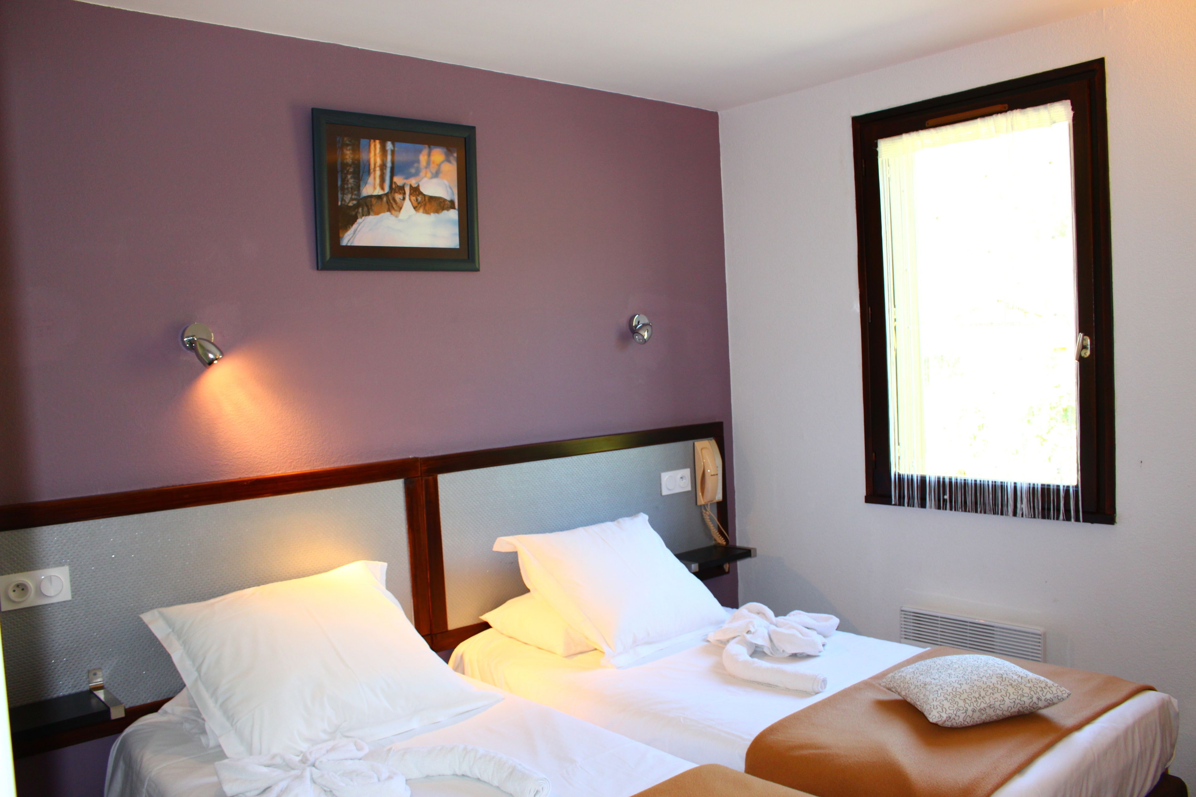 Una camera d'albergo con due letti, una finestra con tende, un quadro appeso al muro e un telefono sul comodino.
