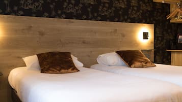 Una cama doble con ropa de cama blanca y dos almohadas marrones, un cabecero de madera y una pared con estampado floral.