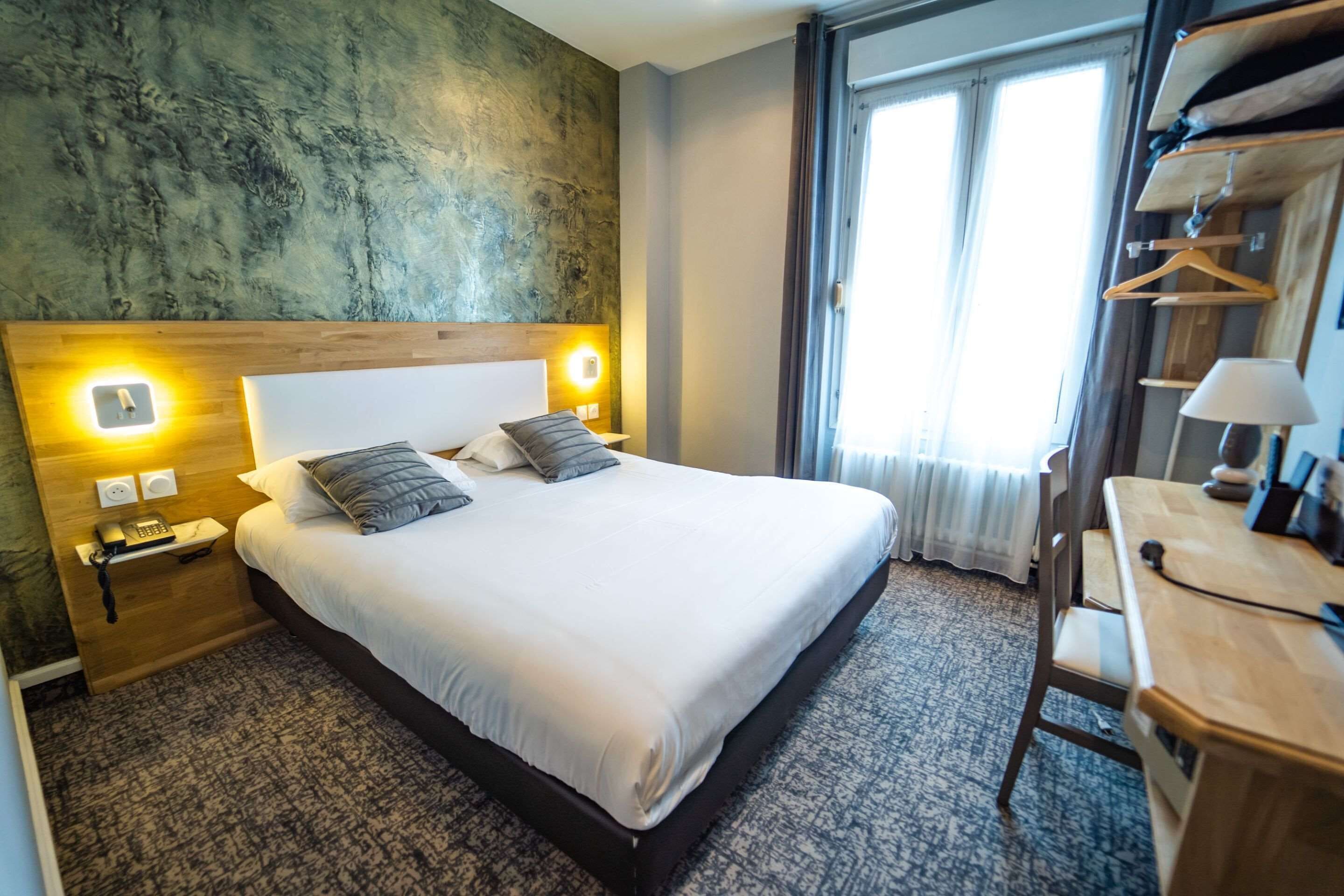 Una habitación de hotel con una cama grande, lámparas de noche, un escritorio y un armario.