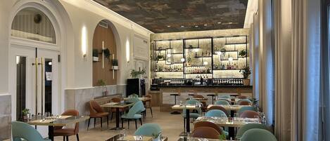 A restaurant with multiple dining tables and chairs, a bar area with shelves of bottles, and a ceiling with a mural.