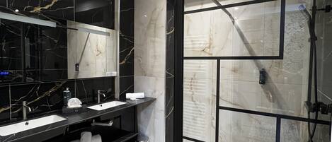 A modern bathroom with two sinks, a glass shower enclosure, and marble walls.