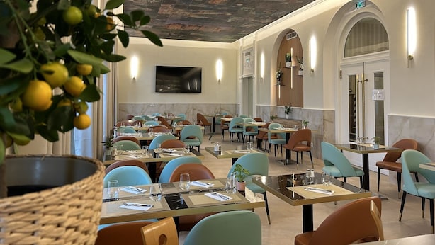 Un restaurante de interior moderno, con un techo decorado con un mural detallado, un televisor de pantalla plana en la pared y diversas opciones de asientos, incluyendo mesas y sillas.