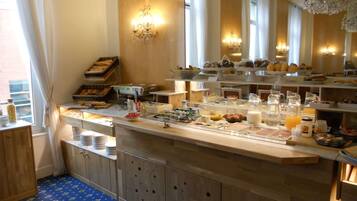 A breakfast buffet with various food items and beverages, wooden cabinets, and a chandelier.