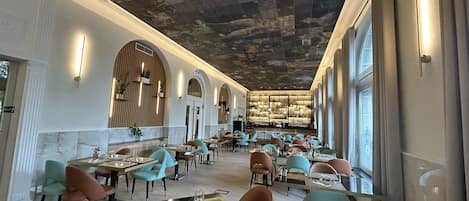 Een ruim restaurant met hoge plafonds, gebogen ramen en diverse zithoeken.