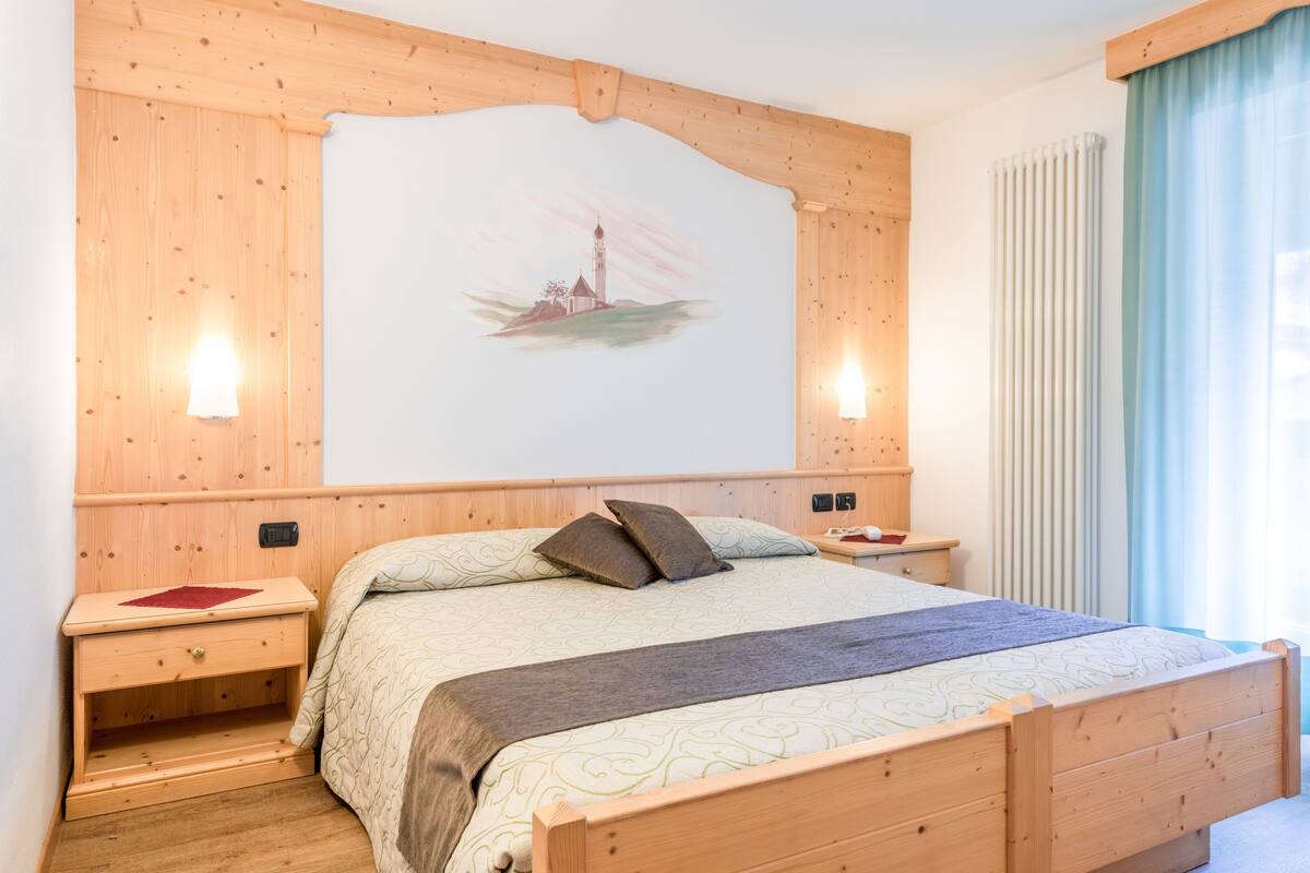 A bedroom with a wooden headboard, a bed with patterned bedding, a nightstand with a lamp, and a wall-mounted artwork of a lighthouse.