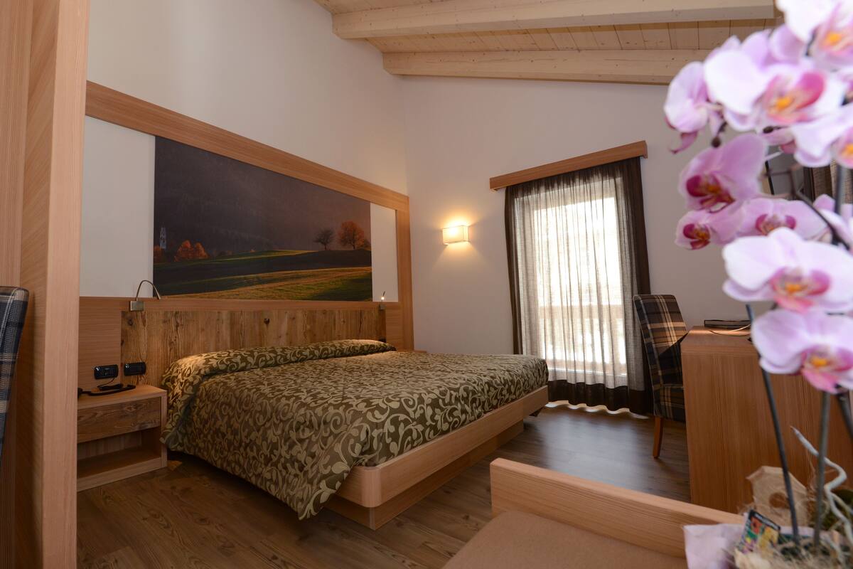 A bedroom with a bed, a desk, a chair, a painting on the wall, and a window with curtains.