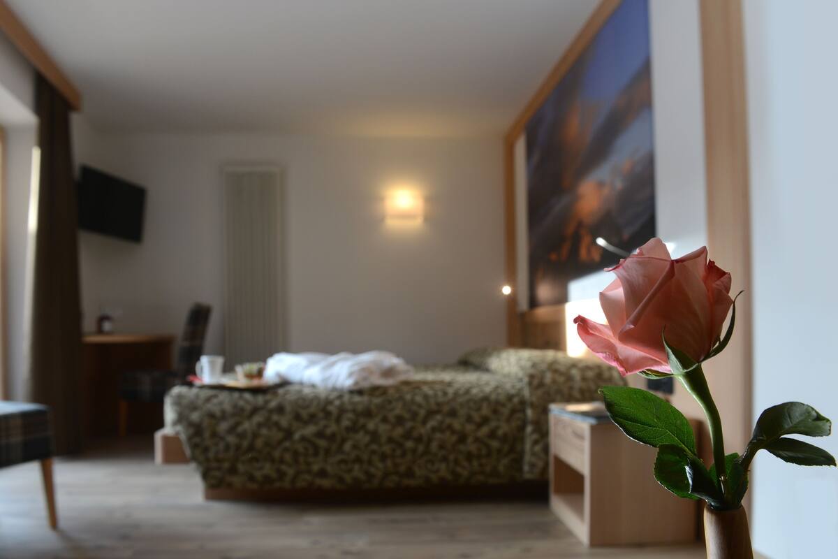 A bedroom with a bed, a bedside table, a chair, a TV mounted on the wall, and a painting on the wall.
