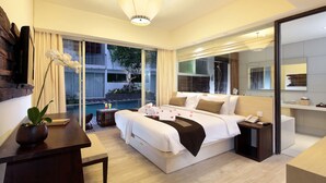 Une chambre d’hôtel moderne avec un grand lit, une table de chevet, un petit bureau, une plante en pot et une vue sur une piscine et un espace extérieur.