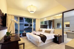 Una habitación de hotel moderna con una cama grande, una mesita de noche, un escritorio pequeño, una planta en maceta y vistas a una piscina y zona exterior.