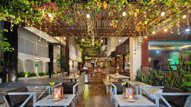 Un restaurant avec des tables et des chaises en bois, un coin bar et un plafond décoré de plantes et de guirlandes lumineuses.
