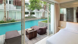 A hotel room with a large bed, a wooden deck, a view of a swimming pool, and a glass door leading to the pool area. - The Akmani Legian (Kuta)