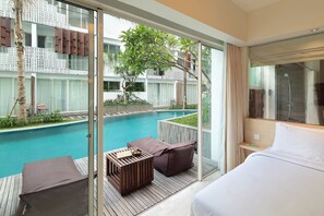 Une chambre d’hôtel dotée d’un grand lit, d’une terrasse en bois, d’une vue sur la piscine et d’une porte vitrée donnant accès à l’espace piscine.