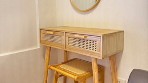 A wooden desk with two drawers and a stool, a round mirror, and a wall-mounted heater.