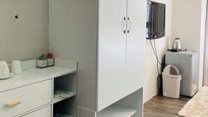 A modern bedroom with a large wardrobe, a small kitchenette, a flat-screen TV, and a decorative wall piece.