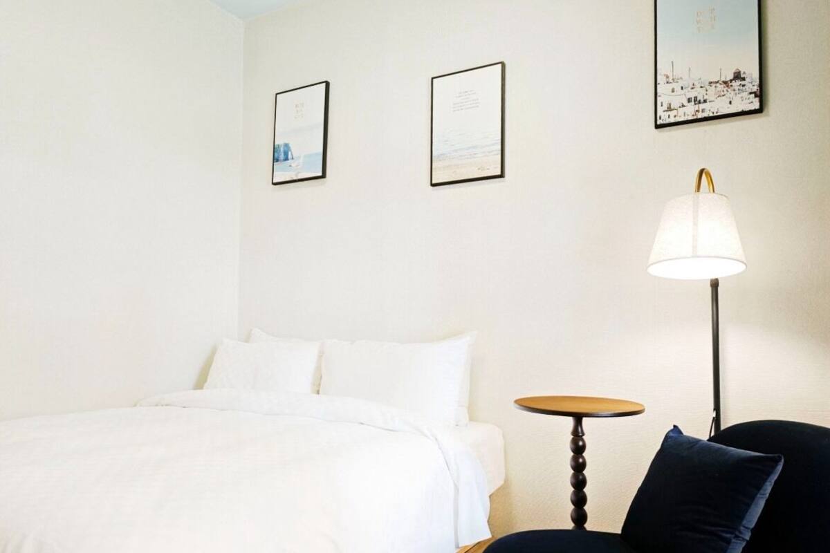 A hotel room with a bed, a small round table, a chair, and a lamp.