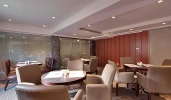Una sala de conferencias moderna con mesas y sillas redondas, paredes de vidrio y un panel de pared de madera.