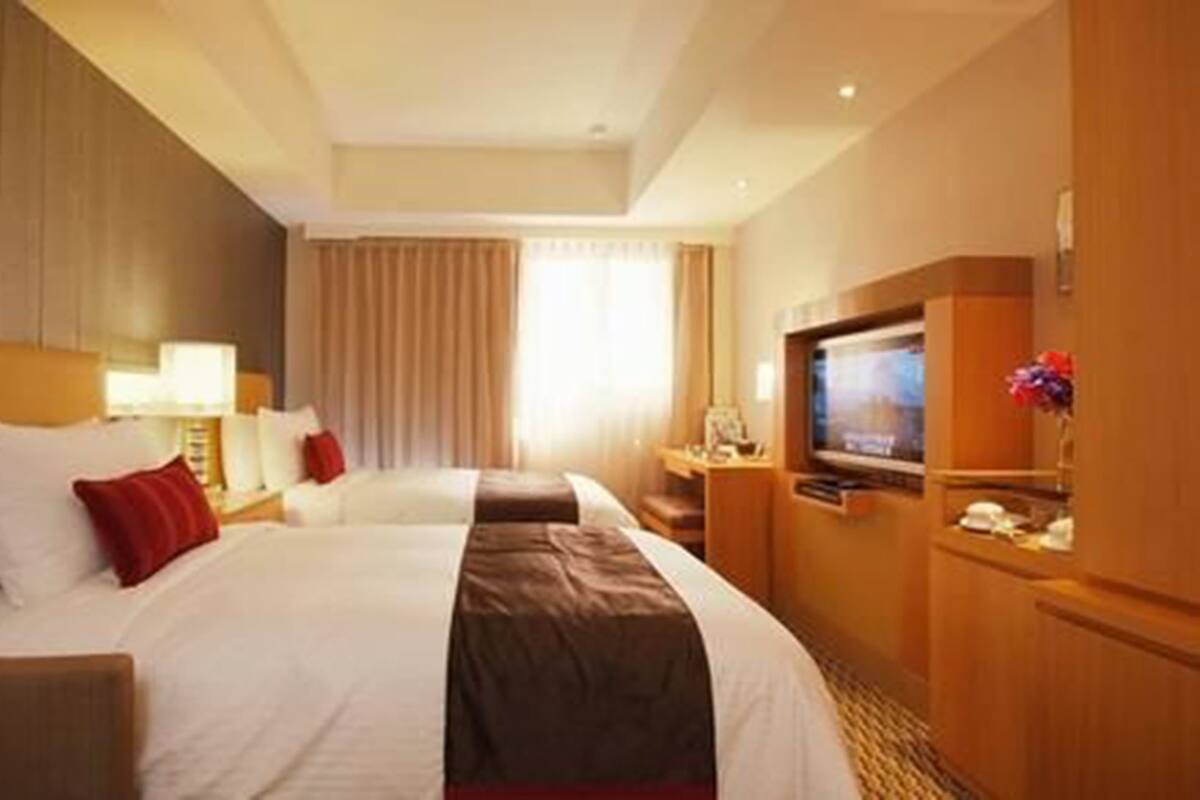 A hotel room with two beds, a TV, and a desk with a lamp.