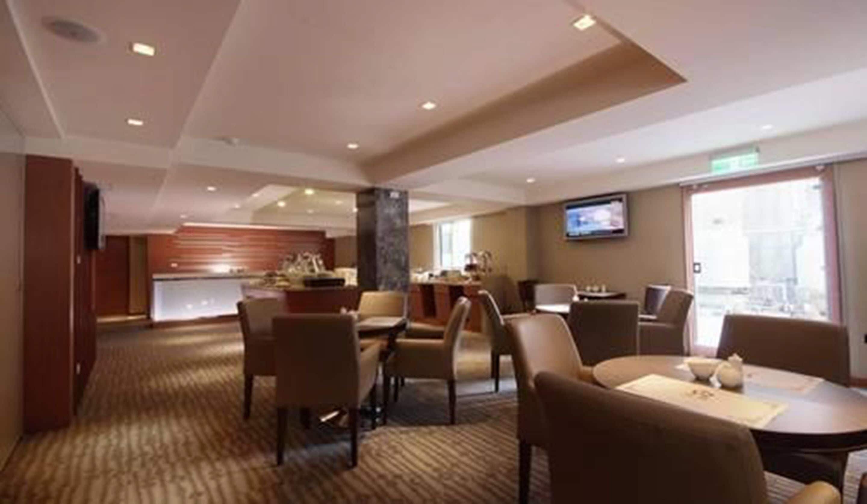 Een hotel lobby met een eetgedeelte, een aan de muur bevestigde televisie en een groot raam dat natuurlijk licht binnenlaat.