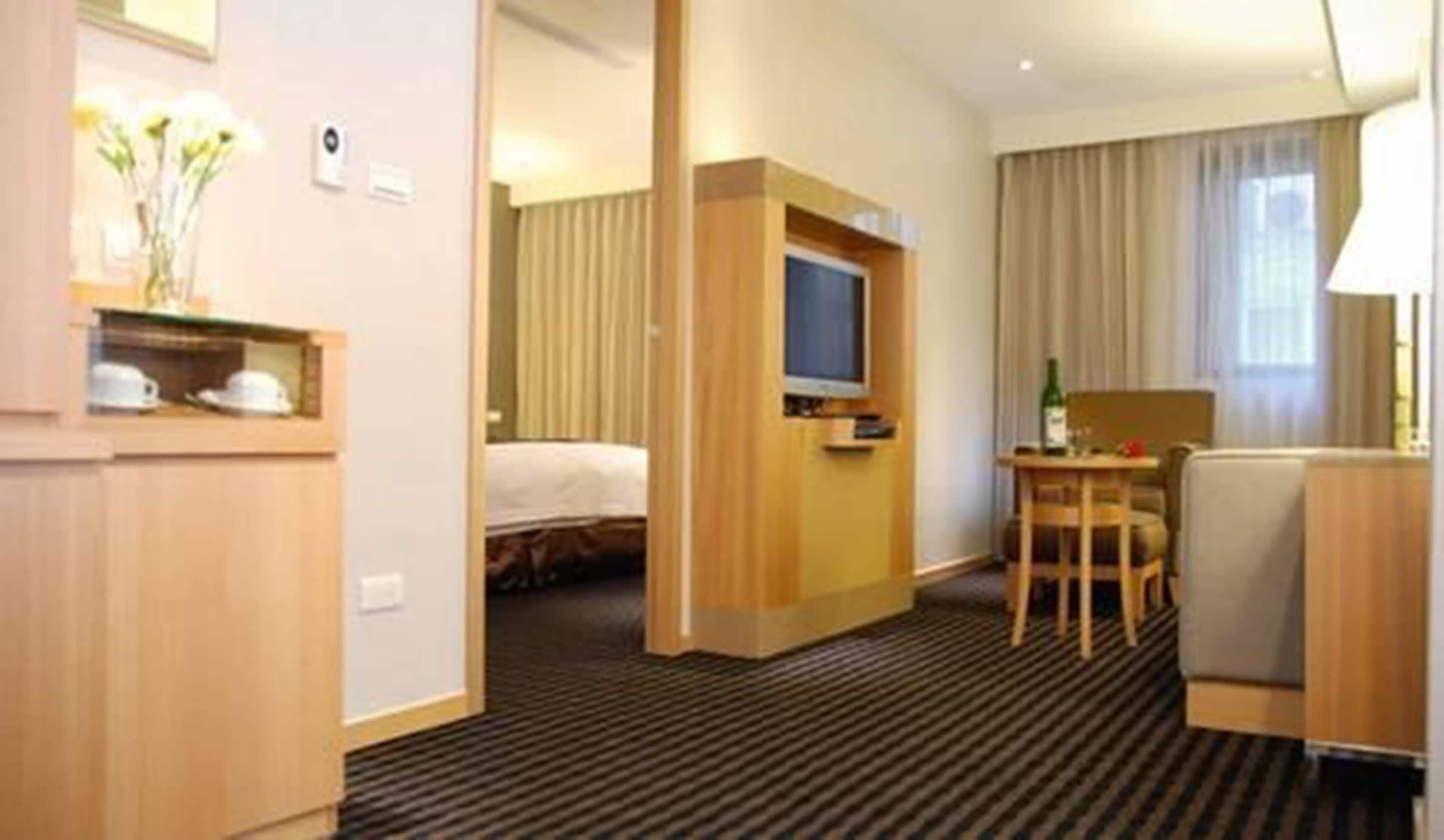 A hotel room with a bed, a desk with a chair, a television, and a small table with a bottle.