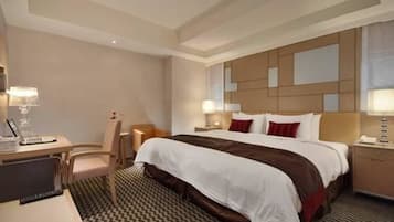 A hotel room with a large bed, a desk, a chair, and two bedside tables with lamps.