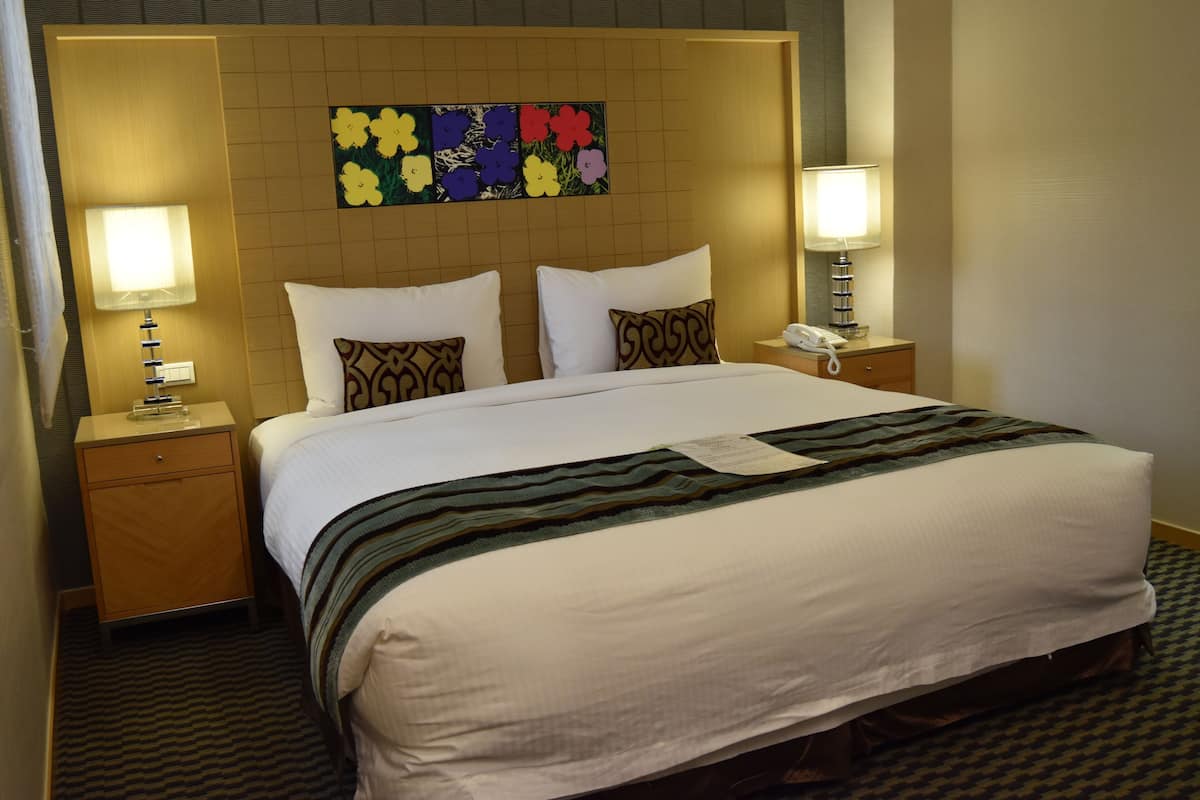 A hotel room with a large bed, two bedside tables with lamps, a wall-mounted telephone, and a floral artwork above the bed.