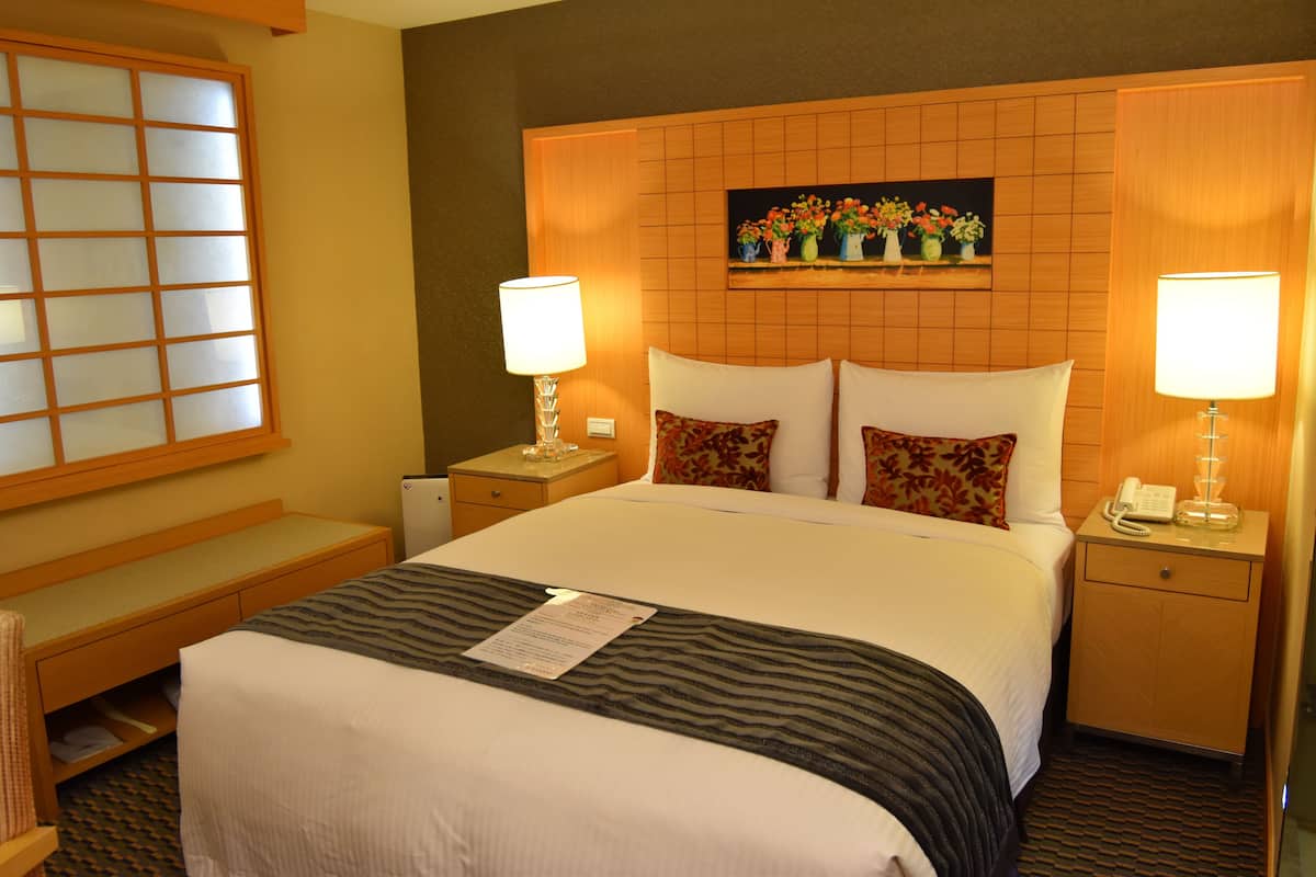 A hotel room with a large bed, two bedside tables with lamps, a small desk, and a window with a view of the outside.