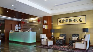 A hotel reception area with a reception desk, seating area, and a wall with a framed sign. - Tokyo International Hotel (Taipei)