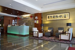 A hotel reception area with a reception desk, seating area, and a wall with a framed sign. - Tokyo International Hotel (Taipei)