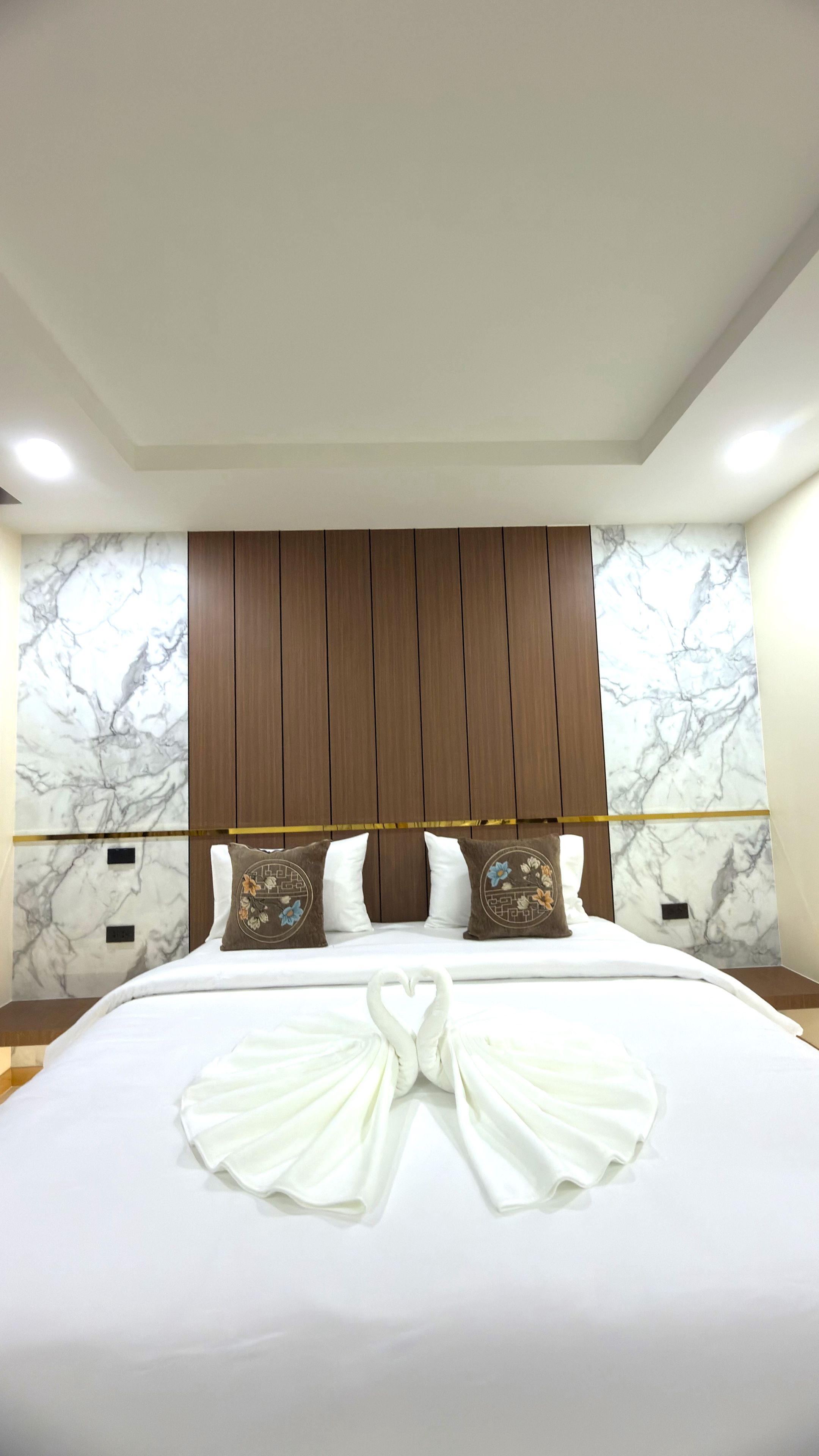 A hotel room with a large bed, wooden headboard, marble wall, and decorative pillows.