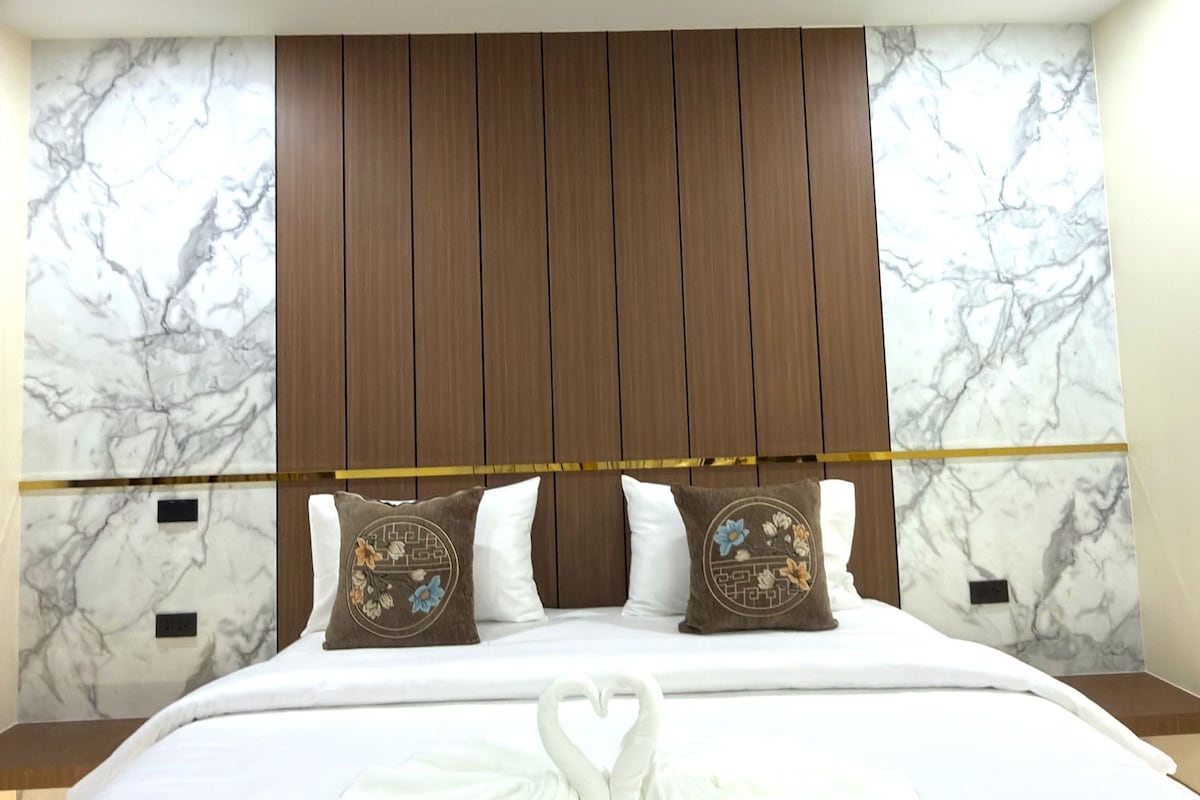 A hotel room with a large bed, wooden headboard, marble wall, and decorative pillows.