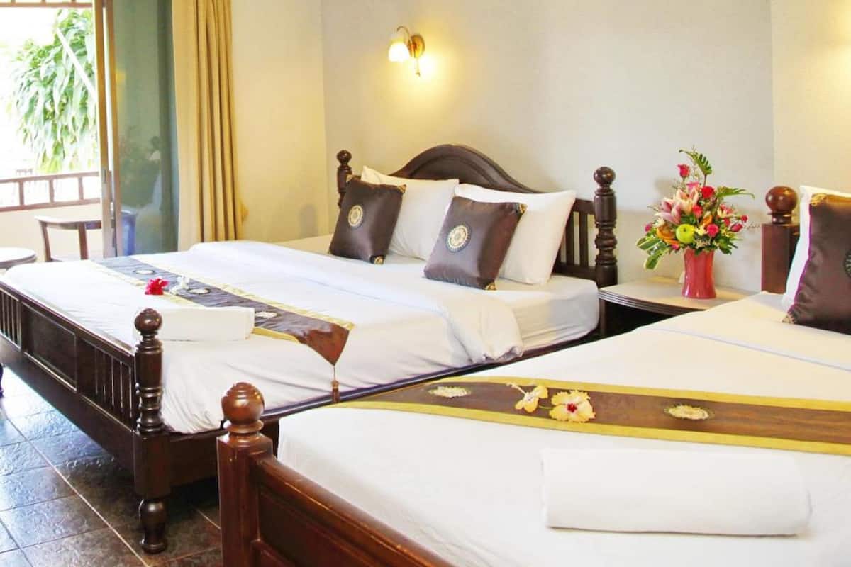 Une chambre d’hôtel avec deux lits, une tête de lit en bois, une petite table sur laquelle est posé un vase de fleurs, et une porte-fenêtre coulissante donnant sur l’extérieur.