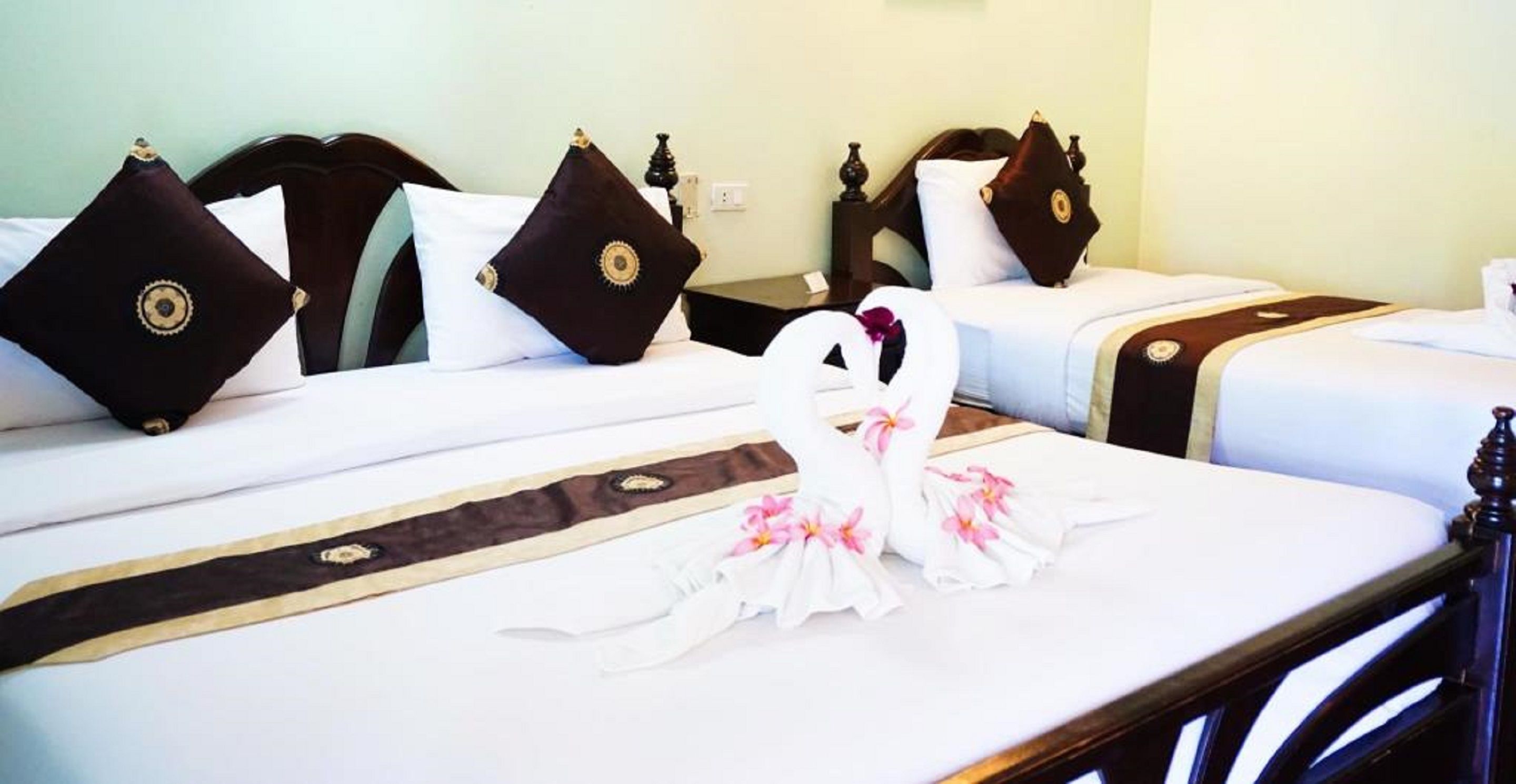 A hotel room with two beds, each with dark headboards and white bedding. There are decorative pillows and a swan-shaped decoration on the bed.