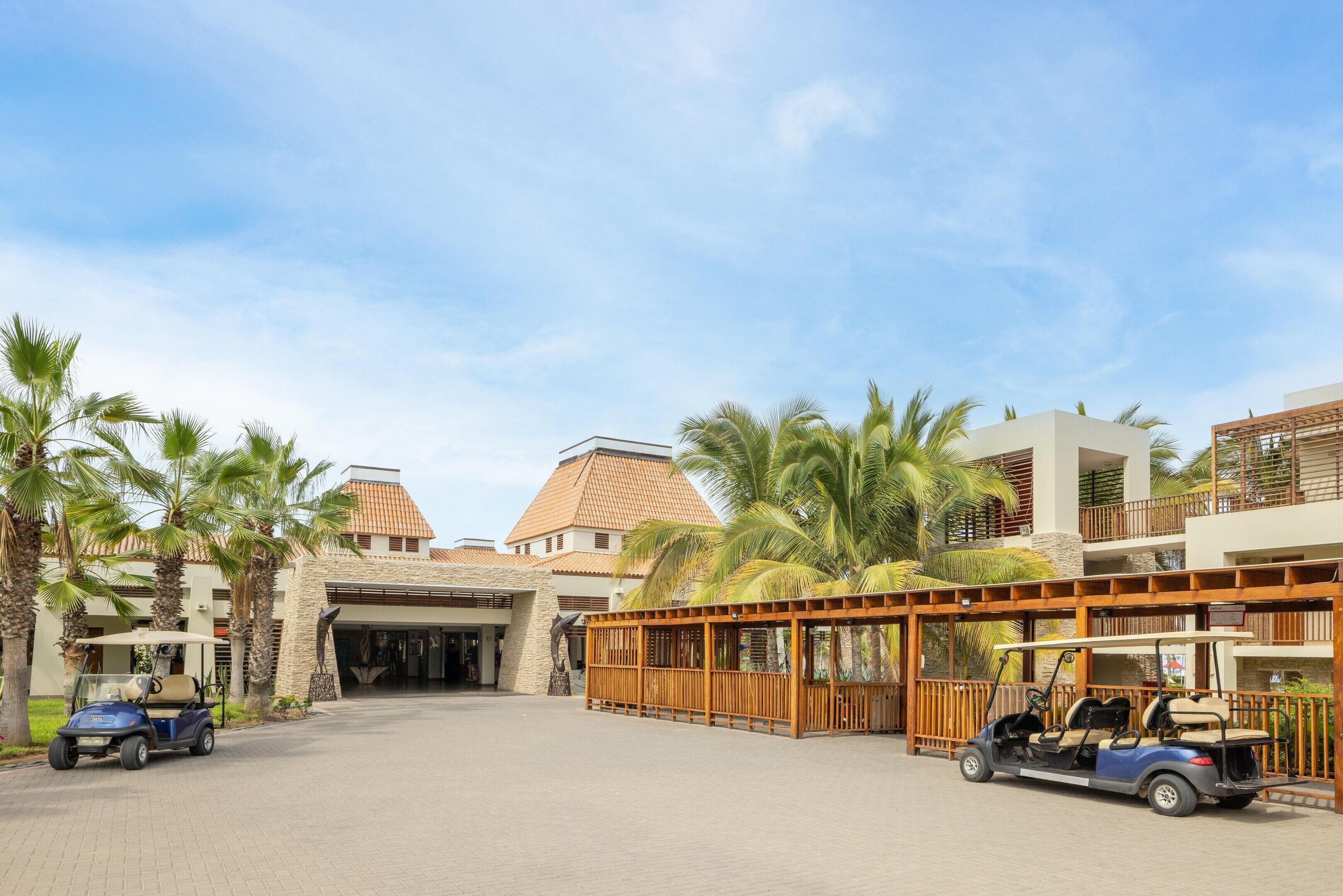 A resort entrance with a paved driveway, palm trees, and a golf cart.