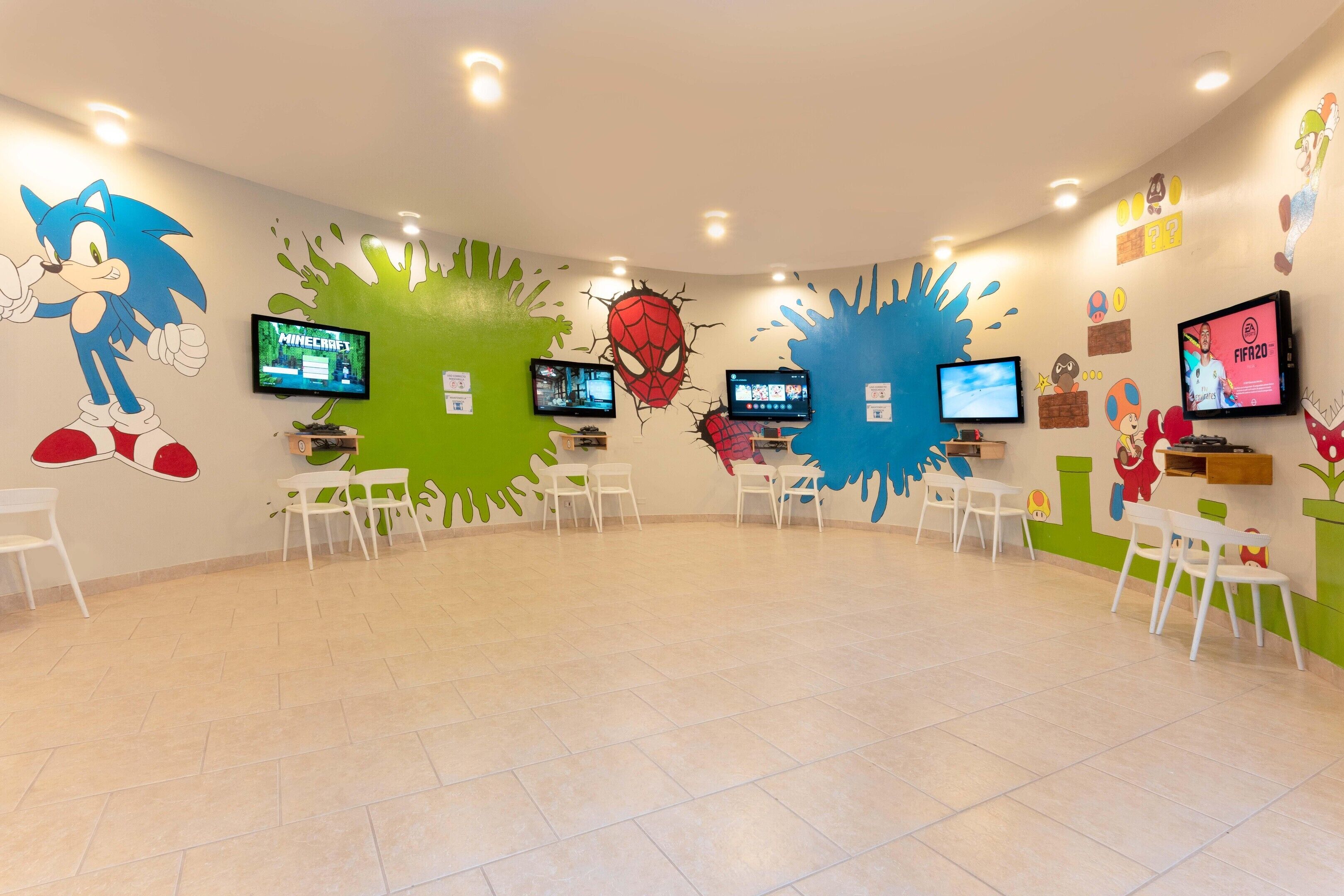 A brightly lit room with multiple gaming consoles and chairs.