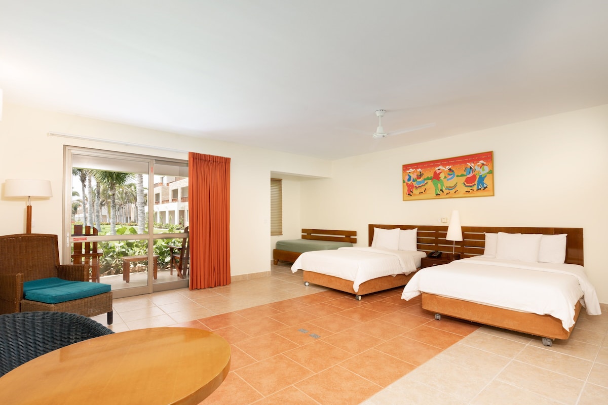 A hotel room with two beds, a dining table, a chair, a sofa, and a balcony with curtains.