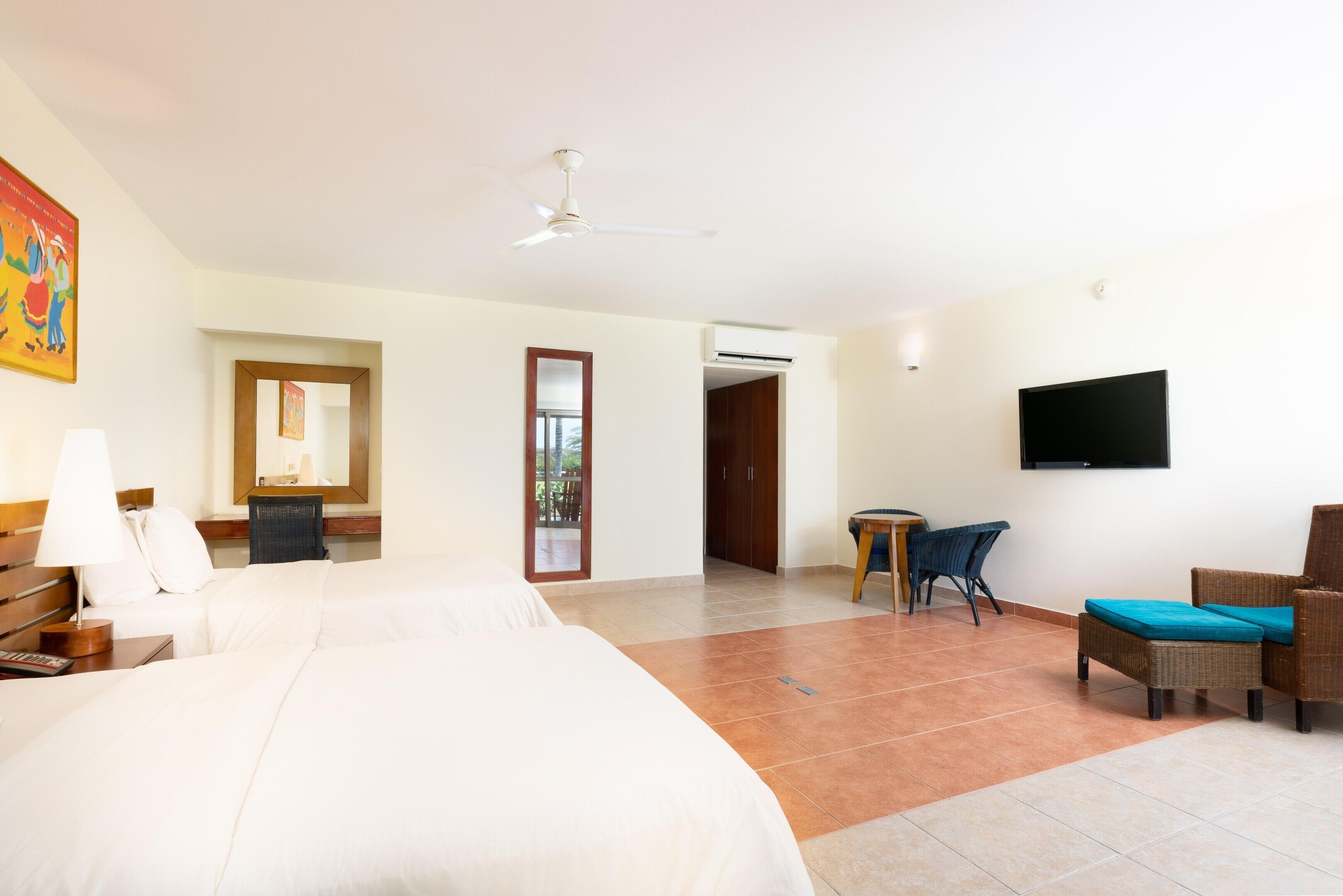 A hotel room with a bed, a desk, a chair, a TV, and an air conditioning unit.