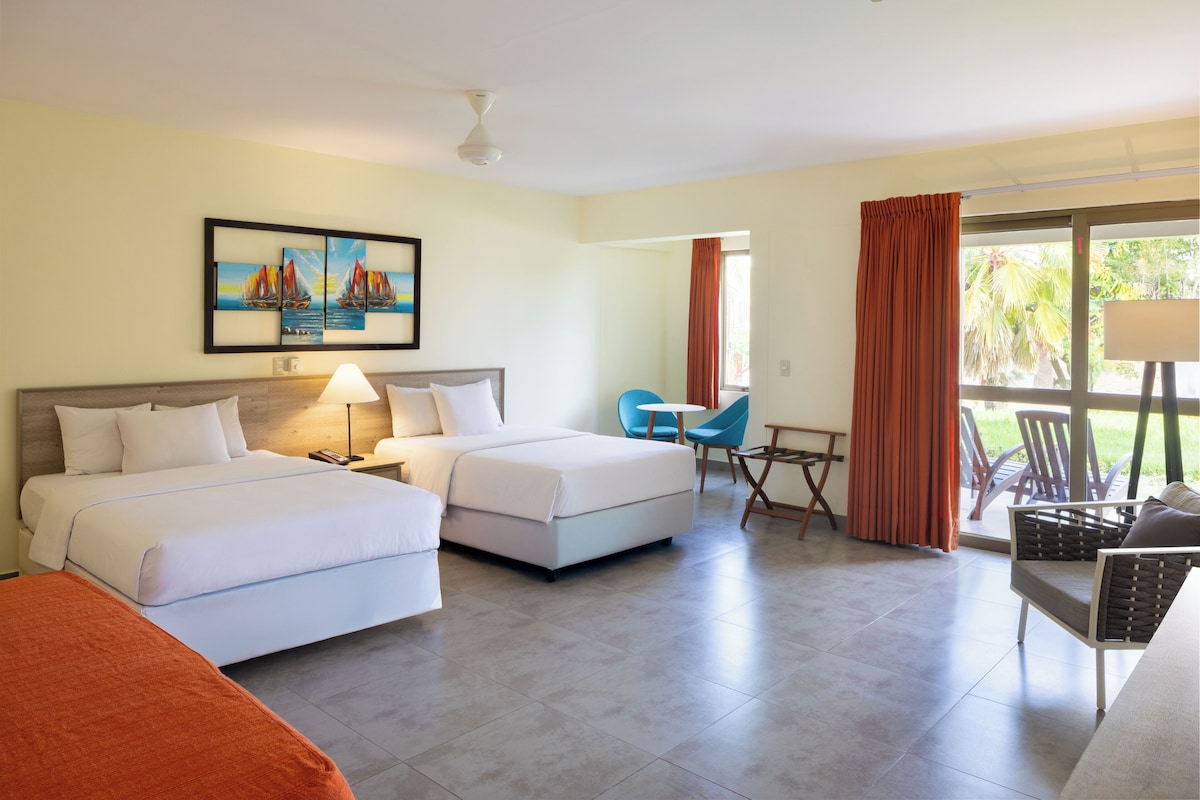A hotel room with two beds, a desk, chairs, and a painting on the wall.