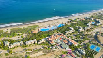 An aerial view of a resort with multiple swimming pools, beachfront, and hotel buildings.