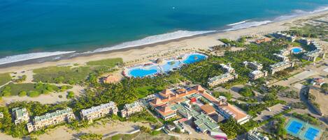An aerial view of a resort with multiple swimming pools, beachfront, and hotel buildings.