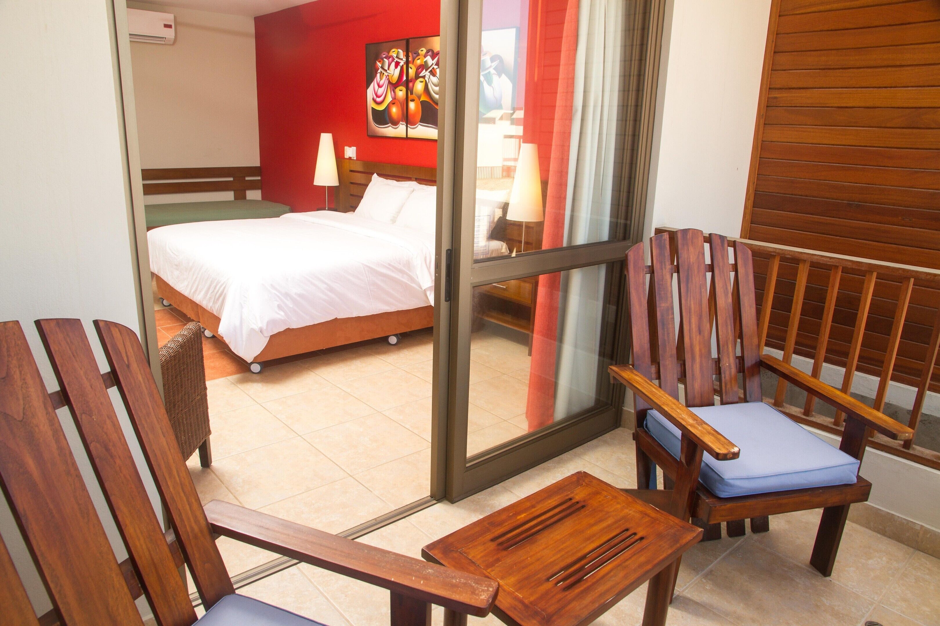 Habitación de hotel con una cama, dos sillas de madera, una mesita y un ventanal corredero que da a otra habitación.